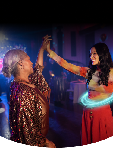 Two women smiling and dancing together at a party, one with a blue ring around her stomach