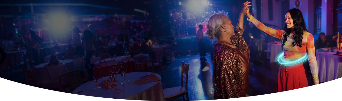 Two women smiling and dancing together at a party, one with a blue ring around her stomach