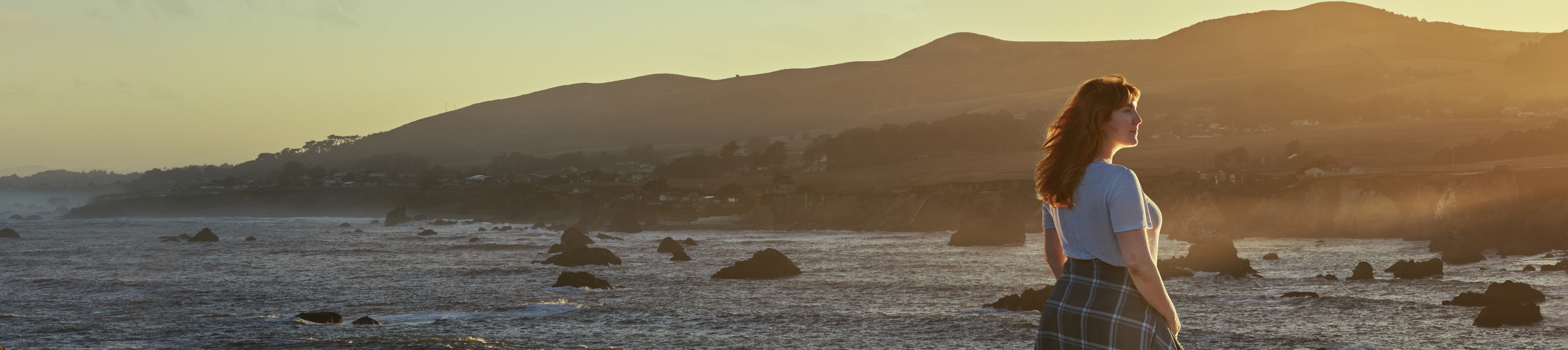 Woman standing by rocky shore at sunset