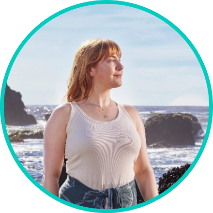 Woman in a white tank top looking out into the distance with the shoreline behind her