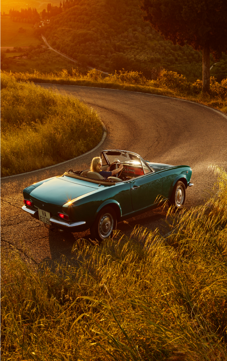 Blue convertible car with a woman driving on a winding road during sunset