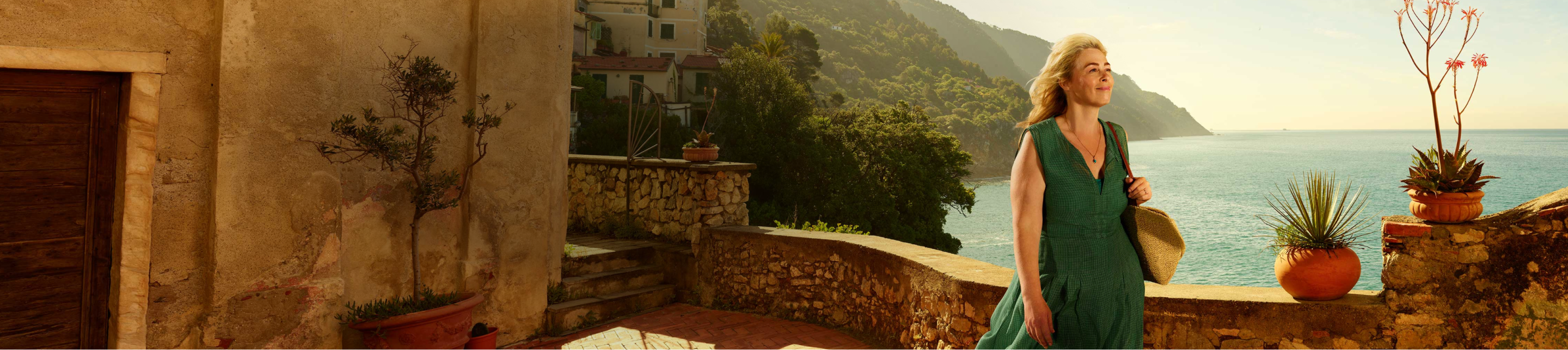 Woman walking on a stone path along the water with mountains in the background